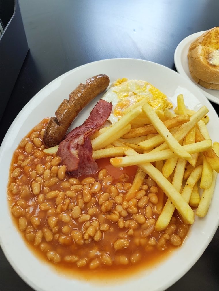 A full breakfast plate of sausages, bacon, scrambled egg, beans and chips